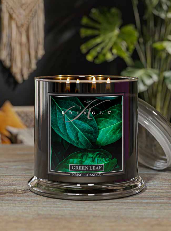 Kringle Candle Green Leaf candle on a wooden surface with decorative leaves.