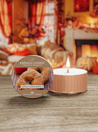 Kringle Candle Apple Cider Donut candle with packaging on a wooden surface, blurred festive background.