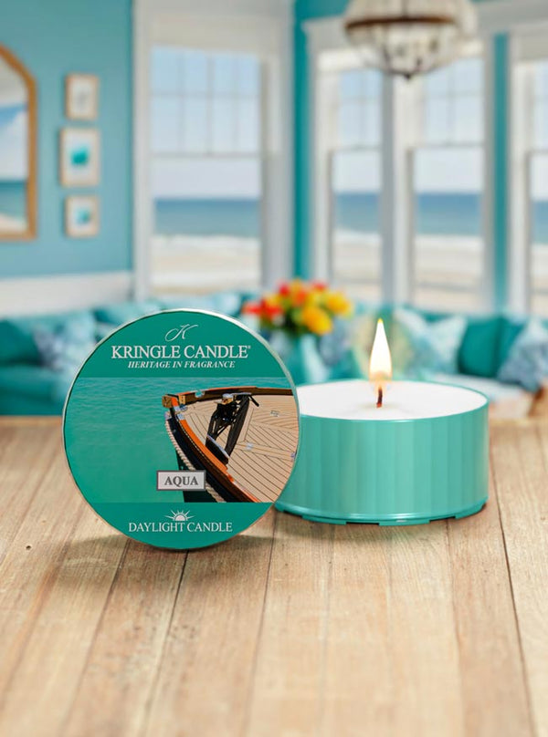 Kringle Candle in Aqua on a wooden surface with a beach-themed room in the background