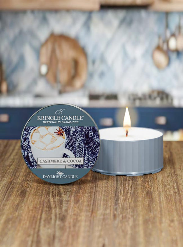 Kringle Candle Cashmere & Cocoa daylight candle on a wooden surface with a kitchen in the background 