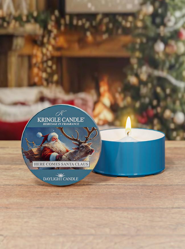 Kringle Candle daytime candle with packaging in front of a festive background with a fireplace and Christmas tree.