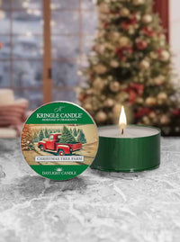 Kringle Candle daylight candle with Christmas tree farm design on a snowy surface with a blurred Christmas tree in the background.