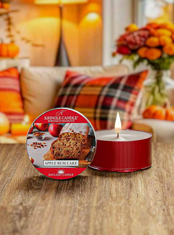 Lit DayLight candle in red cup; label shows sliced apple rum cake with whole apples and spices in the background.