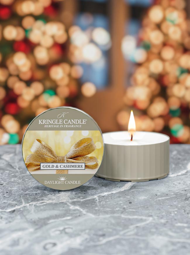 Kringle Candle tin and lit candle on a marble surface with blurred festive lights in the background