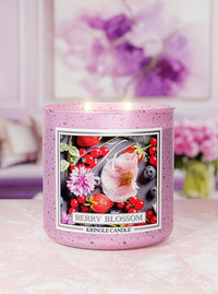 Berry Blossom Kringle Candle on a pink surface with flowers in the background