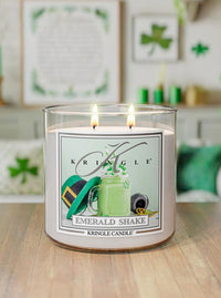 Kringle Candle labeled 'Emerald Shake' on a wooden surface with a festive background.