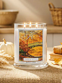 Kringle Candle Amber Wood candle with a scenic design on a table with pumpkins and leaves.