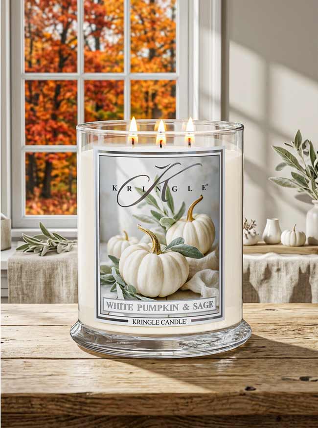 Kringle Candle with a pumpkin and sage design on a wooden surface with autumn foliage outside the window.