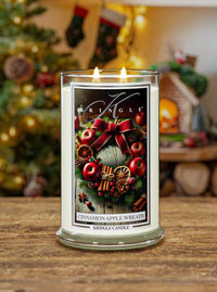 Kringle Candle with 'Cinnamon Apple Wreath' design on a wooden surface with Christmas decorations in the background.