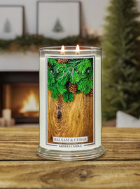 Kringle Candle labeled 'Balsam & Cedar' on a wooden surface with a fireplace in the background