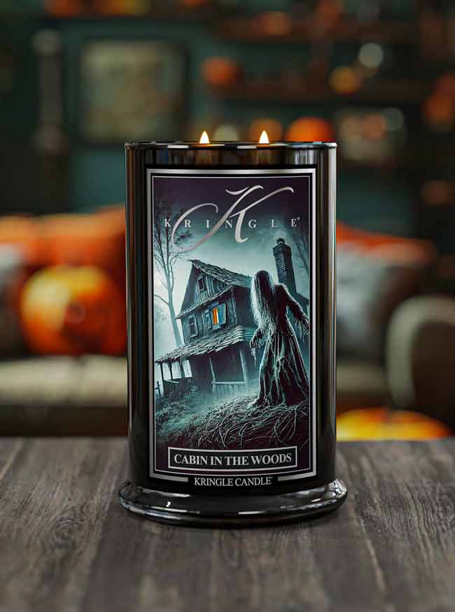 Kringle Candle with 'Cabin in the Woods' design on a wooden surface with blurred pumpkins in the background