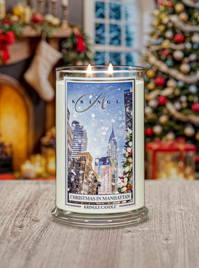 Kringle Candle with Christmas in Manhattan design in front of a decorated Christmas tree and fireplace.