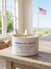 Candle labeled 'American Dream' by Kringle on a wooden surface with a scenic background.