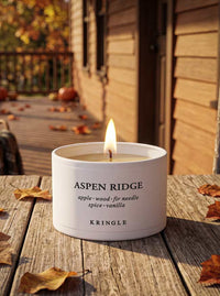 Kringle Candle Aspen Ridge Lit Mini Candle Tin in an outdoor fall setting with leaves and pumpkins.