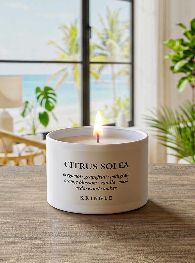 Candle labeled 'Citrus Solea' by Kringle on a table with a window view of greenery