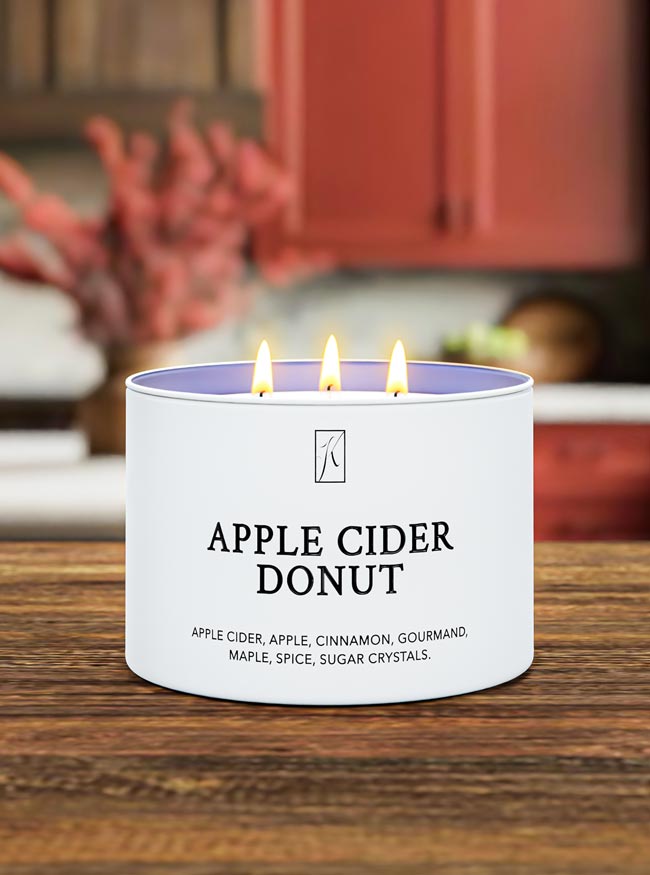 Candle labeled 'Apple Cider Donut' on a wooden surface with a blurred kitchen background