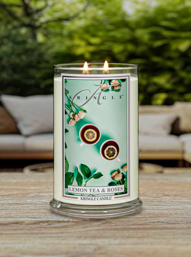 Kringle Candle labeled 'Lemon Tea & Roses' on a wooden surface with a blurred outdoor background.