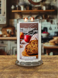 Lit large 2-wick candle with an image of sliced apple rum cake, apples, and nuts on the label.