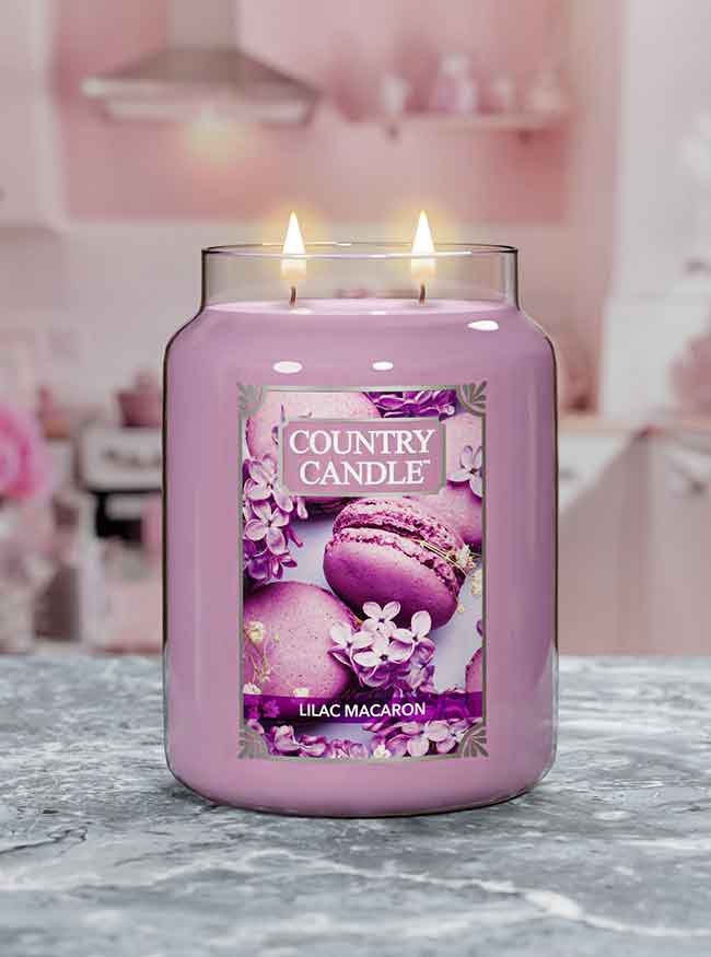 Lilac candle in a glass jar with two flames, labeled "Country Candle Lilac Macaron," set on a kitchen counter.