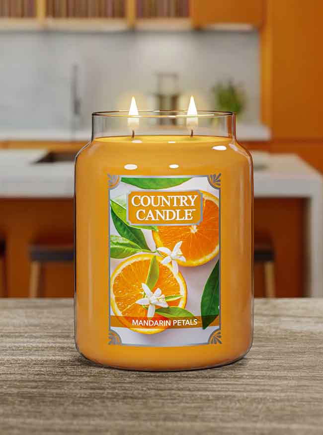 A lit "Mandarin Petals" jar candle labeled "Country Candle" on a table in a modern kitchen setting.
