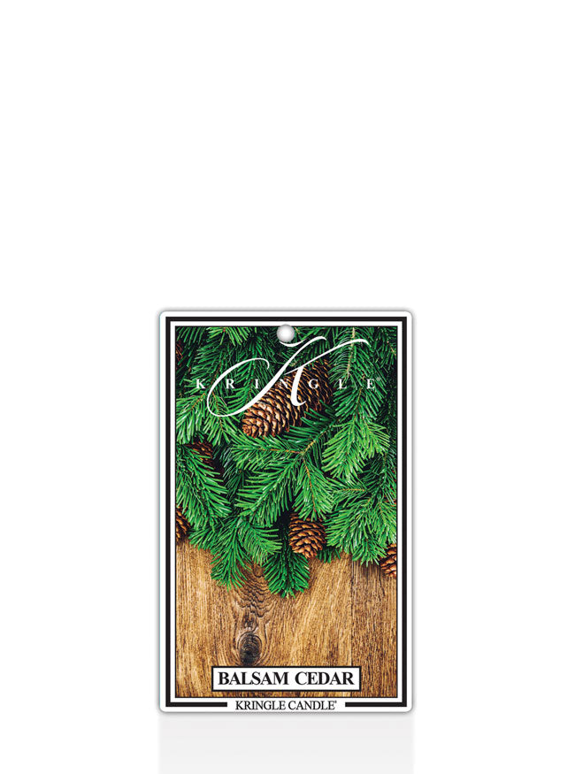 Kringle Candle Balsam Cedar scented air freshener with greenery and pinecones on a white background