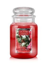 A red jar candle with a Christmas wreath design, labeled 'Christmas Wreath' from Country Candle.
