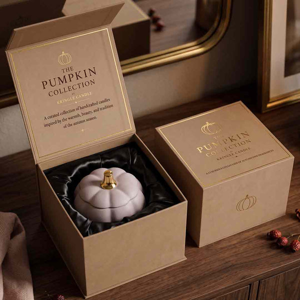 An open kraft gift box reveals a pale lavender pumpkin-shaped candle with a gold top, next to a closed matching box. The inside lid reads 'THE PUMPKIN COLLECTION KINGSLAND CANDLE CO.