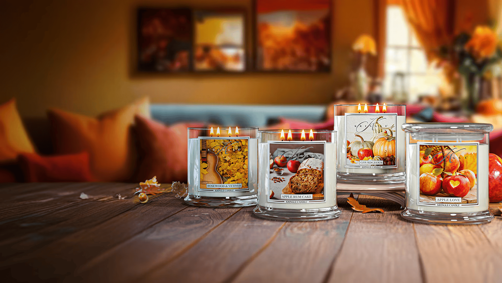 Four candles with autumn-themed labels on a wooden table in a cozy room.