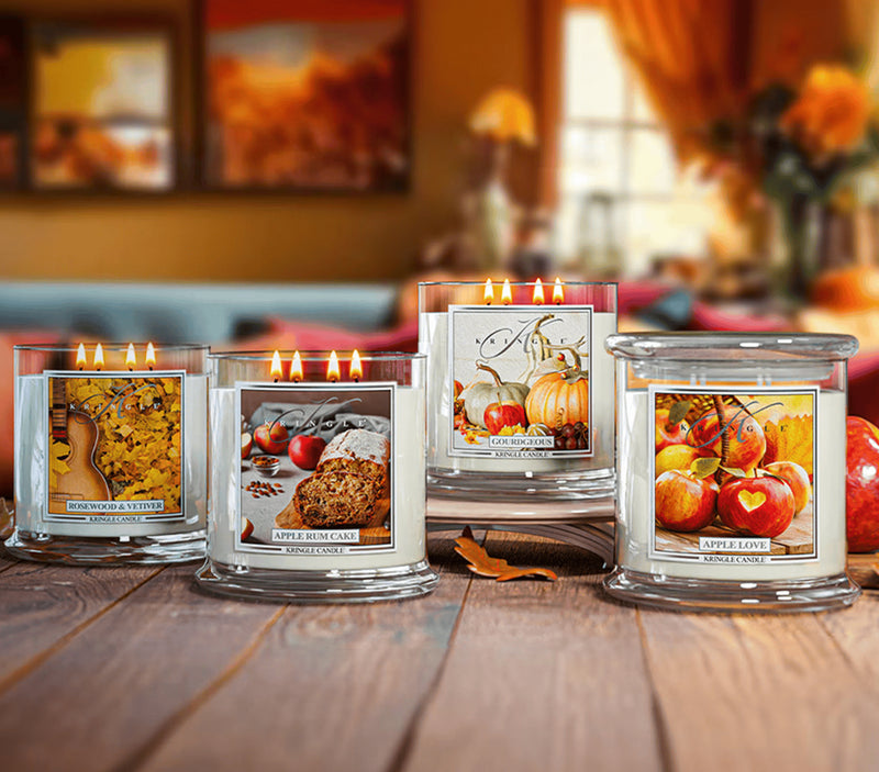 Four scented candles with autumn-themed labels on a wooden surface.