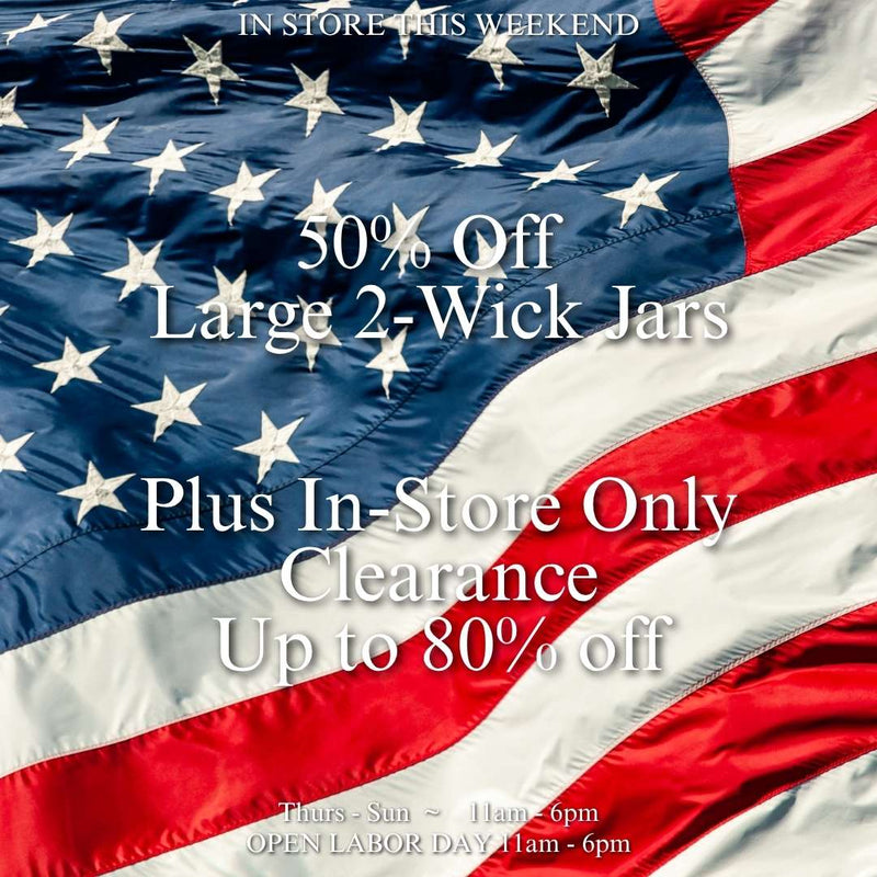 Close-up of a waving American flag with text overlay reading "In Store This Weekend, 50% Off Large 2-Wick Jars, Plus In-Store Only Clearance Up to 80% Off, Thurs-Sun 11am-6pm, Open Labor Day 11am-6pm."