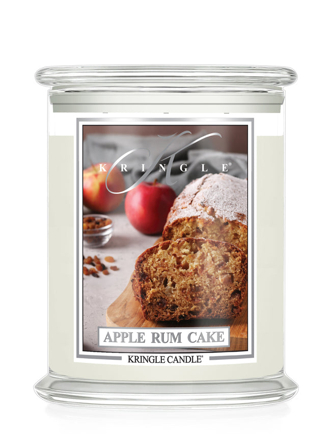 A Kringle Candle jar candle with a clear glass lid and base. The front label features a photo of sliced apple rum cake with apples and spices, and the text 'KRINGLE' and 'APPLE RUM CAKE' plus 'KRINGLE CANDLE'.