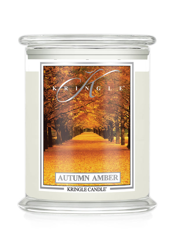 A Kringle Candle in a clear glass jar with cream-colored wax and a front label depicting an autumn tree-lined path. The label reads 'KRINGLE', 'AUTUMN AMBER', and 'KRINGLE CANDLE'.