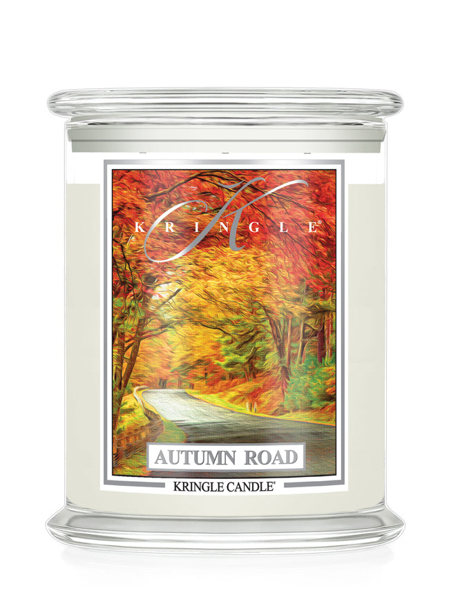 A Kringle Candle jar candle with a clear glass container, cream-colored wax, and a front label depicting an autumn road scene with red, orange, and yellow foliage. The text 'KRINGLE', 'AUTUMN ROAD', and 'KRINGLE CANDLE' are visible on the label.