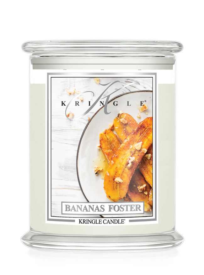 A Kringle Candle jar candle with a clear glass container and a white wax body, featuring a front label for the 'Bananas Foster' scent with a photo of banana slices on a plate.