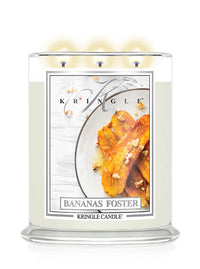 A three-wick scented candle in a clear glass jar with cream-colored wax and a front label reading 'KRINGLE' and 'BANANAS FOSTER.' The label shows roasted bananas on a plate.