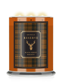 A three-wick scented candle in a cylindrical glass jar with a warm orange-brown body, featuring a black and gold plaid label that reads 'Kringle Reserve' and 'Black Forest Biscotti' with a deer head logo. The candle is shown lit with three glowing flames against a clean white background.