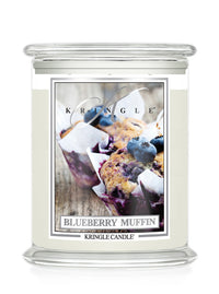 A Kringle Candle jar candle with a clear glass container and a cream-colored wax body. The front label features a photograph of blueberry muffins and reads 'BLUEBERRY MUFFIN' with the brand name 'KRINGLE' at the top.