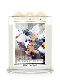A Kringle Candle jar labeled 'Blueberry Muffin' with a clear glass container, cream-colored wax, three lit wicks, and a front label showing blueberry muffins. The brand name 'Kringle' is visible on the label.