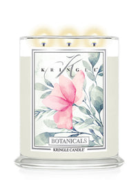 A Kringle Candle 'Botanicals' three-wick soy candle in a clear glass jar, lit with three glowing flames. The front label features a watercolor pink flower and green leaves on a white background.
