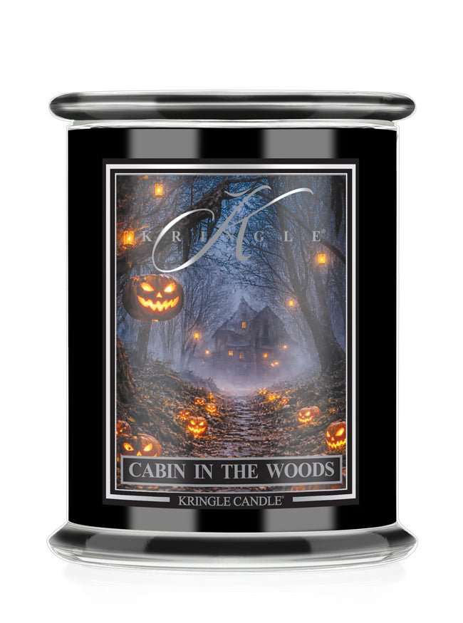A black glass jar candle with a clear lid, featuring a Halloween-themed label that reads 'Cabin in the Woods' and shows a haunted forest scene with glowing jack-o'-lanterns. The brand name 'Kringle Candle' is visible on the label.