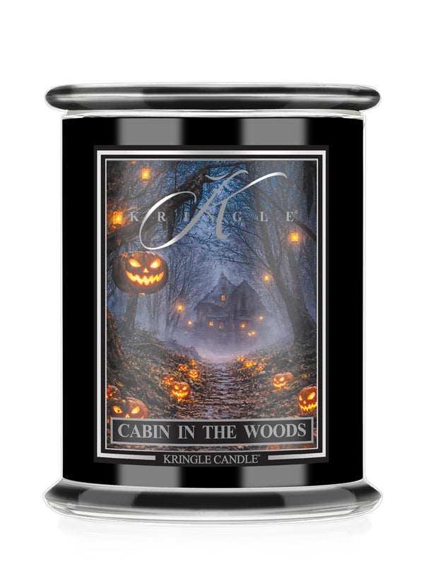 A black glass jar candle with a clear lid, featuring a Halloween-themed label that reads 'Cabin in the Woods' and shows a haunted forest scene with glowing jack-o'-lanterns. The brand name 'Kringle Candle' is visible on the label.