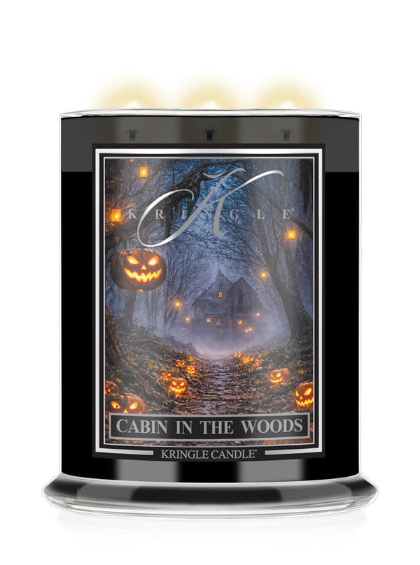 A black glass jar candle with three lit wicks, featuring a Halloween-themed label that reads 'Cabin in the Woods' and shows a haunted forest scene with glowing jack-o'-lanterns. The brand name 'Kringle Candle' is visible on the label.