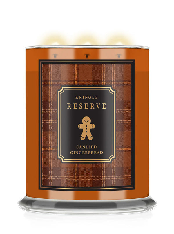 A Kringle Reserve 'Candied Gingerbread' scented candle in a tall amber glass jar with a black and brown plaid label featuring a gingerbread man illustration, shown with three lit wicks on a white background.