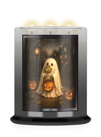A CANDY HAUL scented candle in a cylindrical glass jar with a black base and a clear top, featuring a Halloween-themed graphic of a ghost holding a jack-o'-lantern on the front label. Three candles are lit at the top, casting a warm glow against a white background.