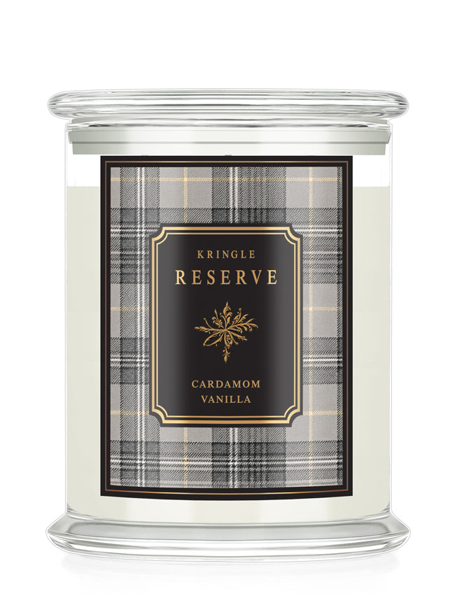 A Kringle Reserve candle in a clear glass jar with a white wax fill and a front label featuring a black and gray plaid pattern with gold lettering that reads 'Kringle Reserve Cardamom Vanilla'.