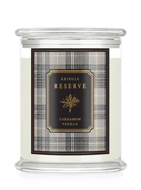 A Kringle Reserve candle in a clear glass jar with a white wax fill and a front label featuring a black and gray plaid pattern with gold lettering that reads 'Kringle Reserve Cardamom Vanilla'.