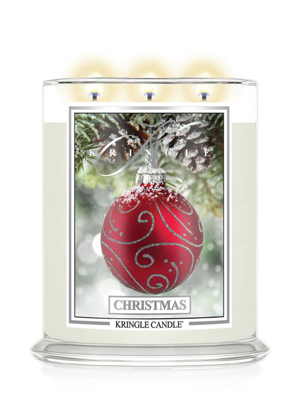 A Kringle Candle 'Christmas' scented candle in a clear glass jar with three lit wicks, featuring a front label with a red ornament and pinecone design on a white background.
