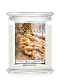 A Kringle Candle jar candle labeled 'Christmas Cashmere' with a warm-toned label showing a cozy winter scene with a tree, window, and fluffy cream throw blanket, on a white background.