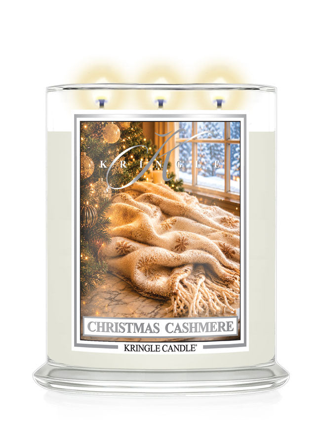 A Kringle Candle three-wick jar candle labeled 'Christmas Cashmere' with a warm-toned winter scene photo on the front. The candle is shown lit with soft glowing flames against a clean white background.
