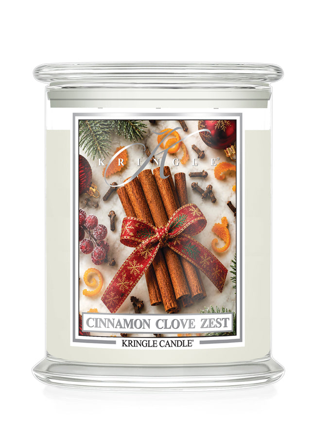 A Kringle Candle jar candle with a clear glass lid and base, filled with off-white wax. The front label features a festive holiday design with cinnamon sticks tied in a red patterned ribbon, cloves, evergreen branches, and citrus slices, with the text 'CINNAMON CLOVE ZEST' and 'KRINGLE CANDLE' visible.